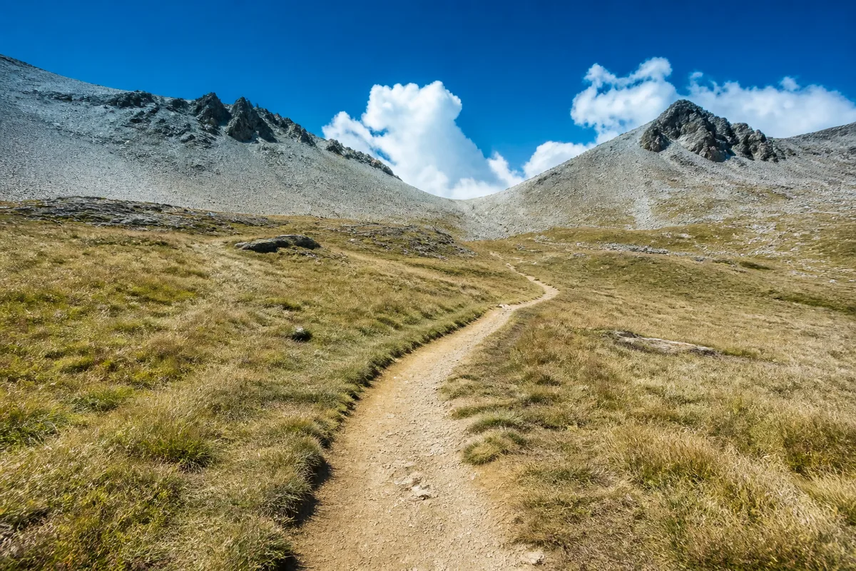 Sentier de terre serpentant dans un alpage vide vers un col minéral